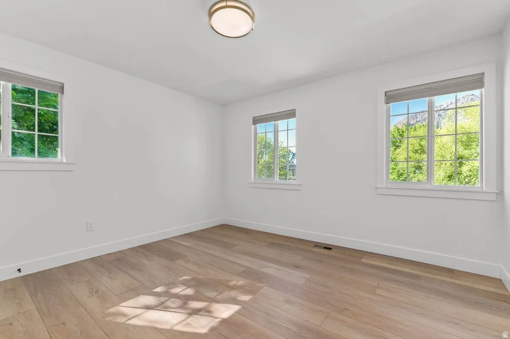 Bright room featuring multiple windows with roller shades, wood-finish flooring, white walls, and a flush-mount ceiling light