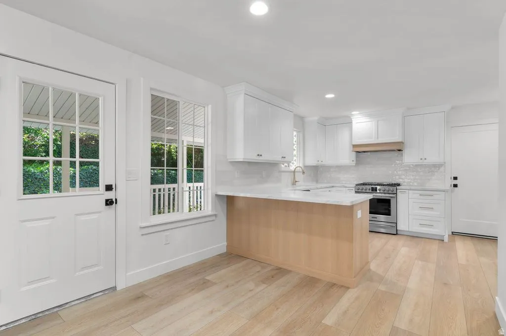 Modern kitchen featuring white cabinetry, light wood-finish flooring, a central island with a light-toned wood base, stainless steel appliances, and an intricate tile backsplash