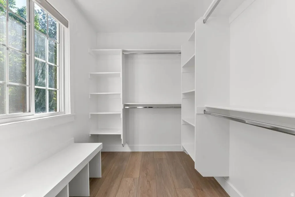 Walk-in closet featuring built-in shelving, hanging rods, an integrated window, a built-in bench, and wood-finish flooring