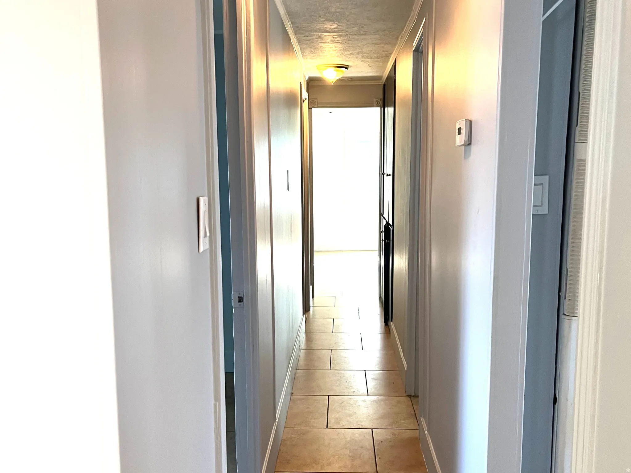 Hallway featuring light-toned tile flooring, light gray walls, and multiple ceiling-mounted flush light fixtures