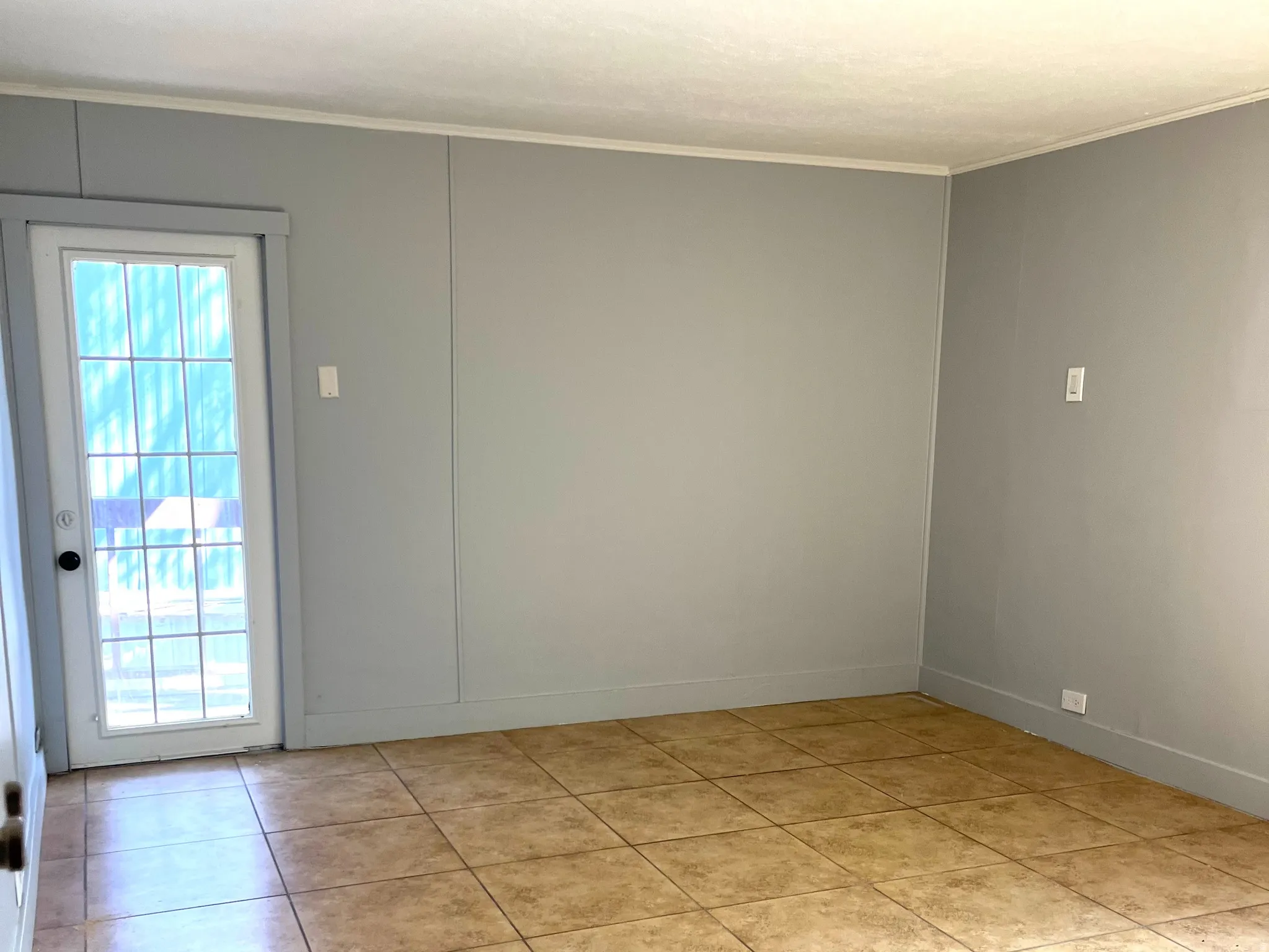 Spacious interior room featuring light-colored tile flooring, neutral wall tones, and a rear exit door with multiple window panes