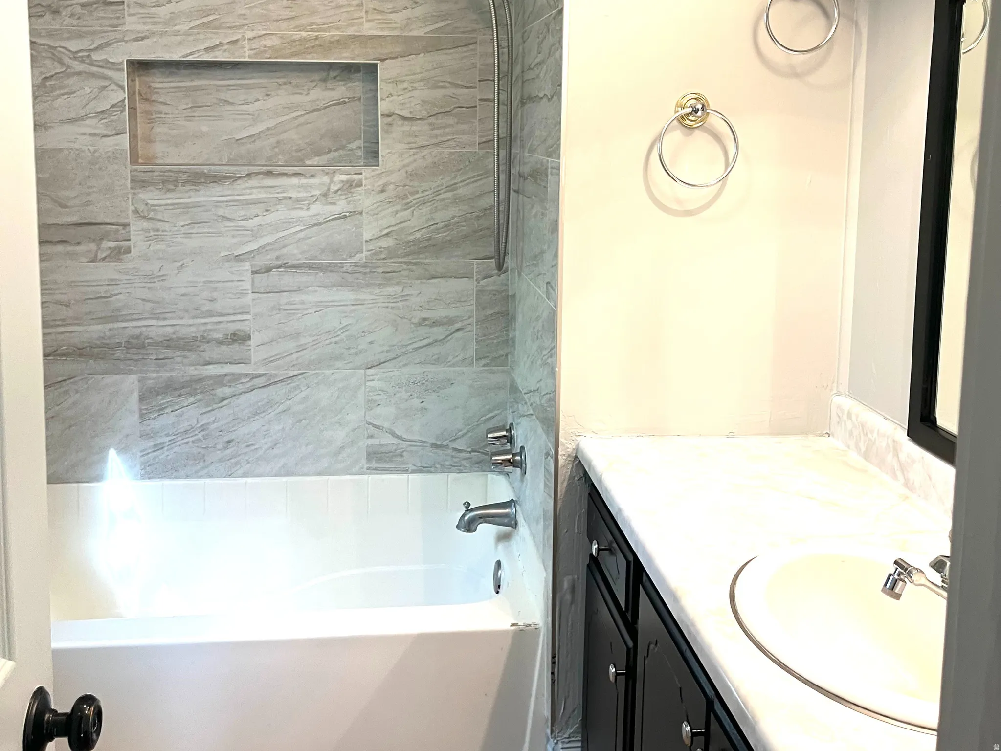 Bathroom featuring a white bathtub with a tiled shower surround, recessed shower niche, and a shower/tub combination faucet with a handheld showerhead