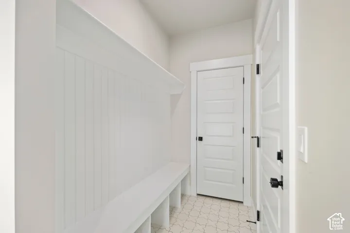 Built-in bench seating with cubby storage, vertical panel wall treatment, white paneled doors with black hardware, and patterned floor tiling