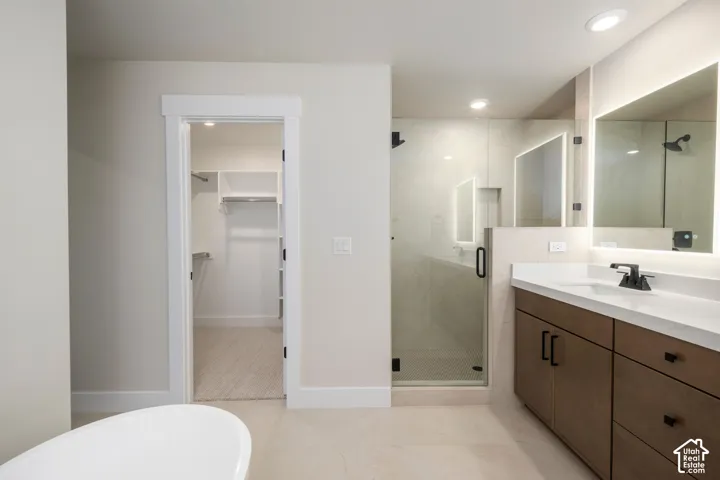Bathroom featuring a glass-enclosed shower, dual vanity with undermount sinks, illuminated mirrors, and a freestanding soaking tub