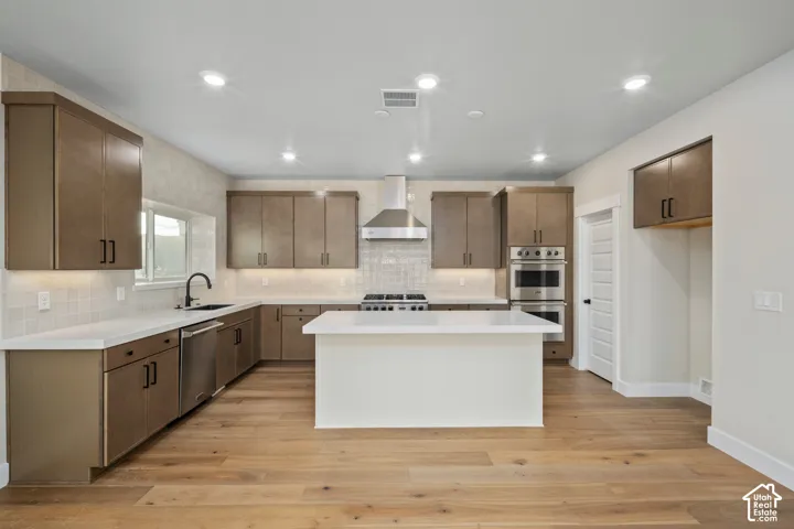 Contemporary kitchen featuring a central island with a white countertop, wood-finish flooring, recessed lighting, and stainless steel appliances