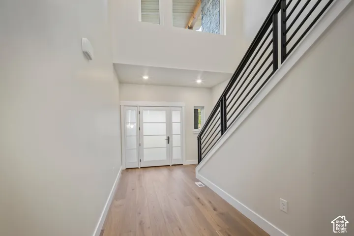 Entryway featuring light wood-finish flooring, a contemporary black metal baluster staircase, recessed lighting, and white French doors with frosted glass panels