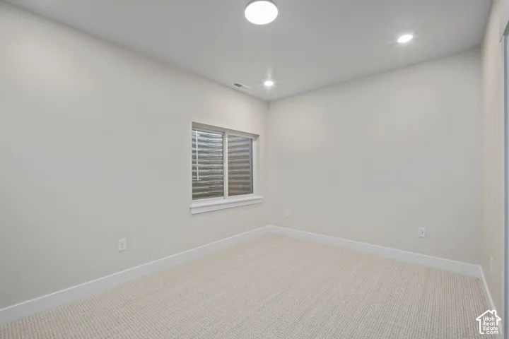 Neutral-toned room featuring a single window with blinds, carpet flooring, and recessed ceiling lighting