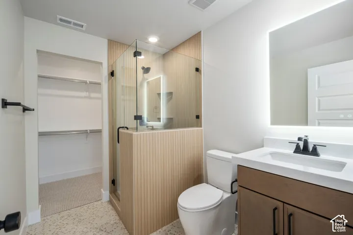 Modern bathroom featuring a glass-enclosed shower with wood-paneling, a floating vanity with a white countertop and dark hardware, an illuminated mirror, and a walk-in closet with built-in shelving