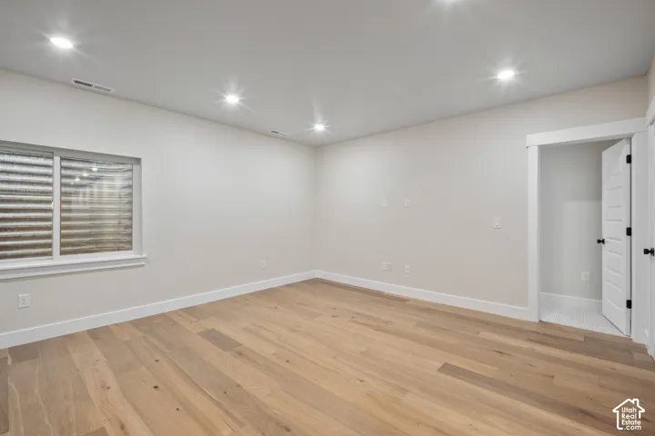 Spacious room featuring light wood-finish flooring, recessed ceiling lighting, and white baseboards