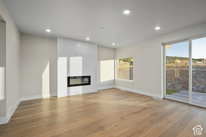 Spacious living area featuring wood-finish flooring, a contemporary linear electric fireplace with shiplap surround, recessed lighting, and large windows with sliding glass door access to the exterior