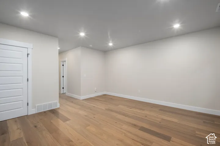 Spacious room featuring light-toned wood-finish flooring, recessed lighting, white baseboards, and a paneled white door