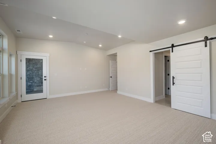 Spacious room featuring neutral carpeting, recessed lighting, white trim, a barn door with black hardware, and a glass-paneled door