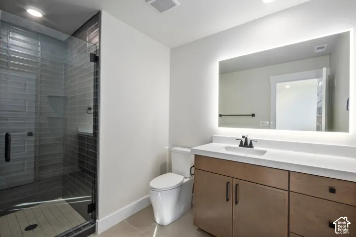 Bathroom featuring a glass-enclosed shower with horizontal gray tile, a light wood-finish vanity with ample storage, a white countertop, a rectangular undermount sink, and an illuminated mirror
