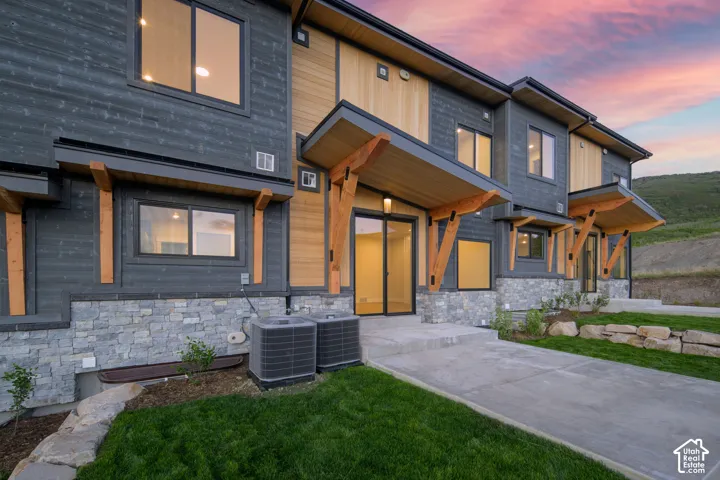 Modern architectural exterior featuring mixed materials including dark horizontal siding, light wood-finish accents, and a stacked stone base