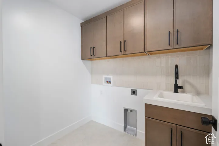 Laundry area featuring wood-finish cabinetry, a built-in utility sink with a matte black faucet, and a tiled backsplash