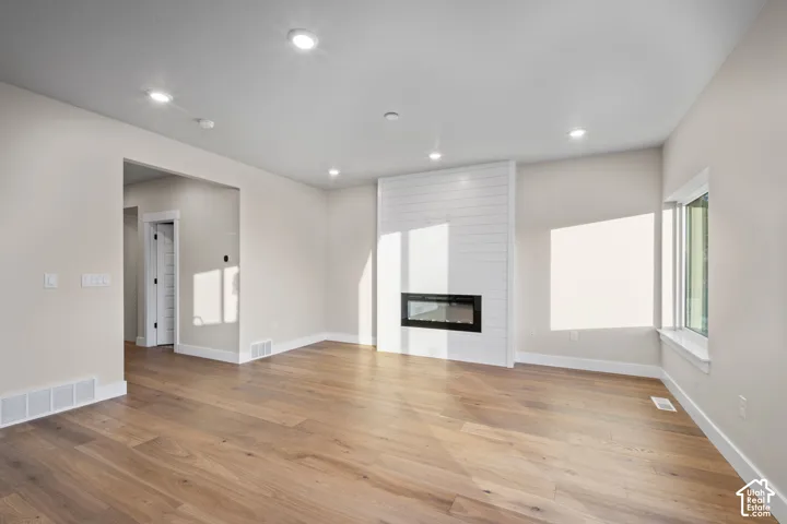 Spacious room featuring wood-finish flooring, recessed lighting, and a contemporary linear fireplace with a shiplap surround
