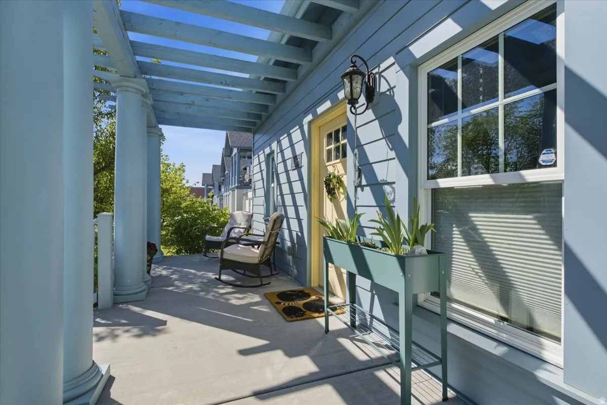 Covered front porch featuring architectural columns, a pergola, siding exterior, a multi-pane entry door, and an exterior wall sconce