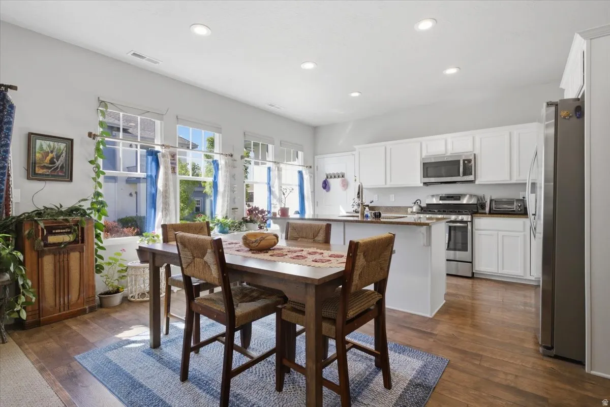 Open-concept kitchen and dining area featuring wood-finish flooring, white cabinetry, recessed lighting, and multiple windows providing ample natural light