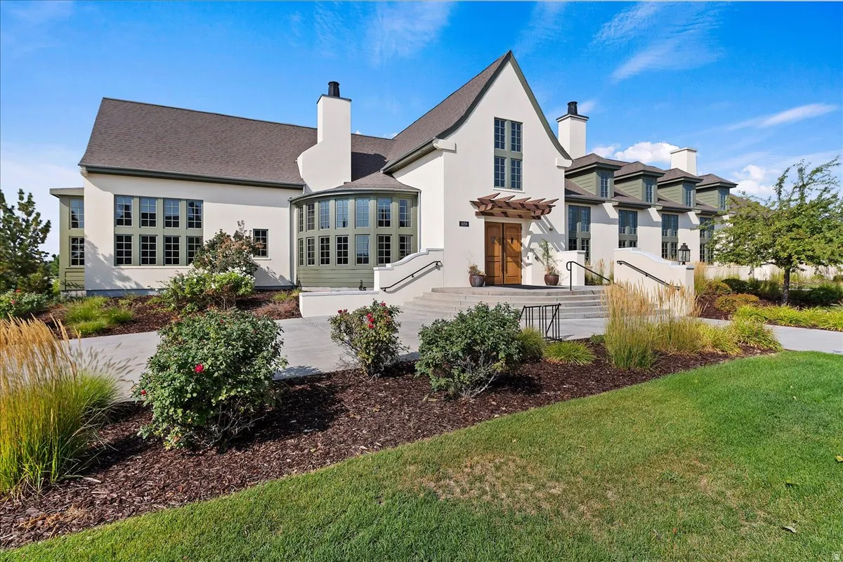 Stucco exterior with multiple gables and dormers, featuring a prominent entrance with wood double doors under a pergola