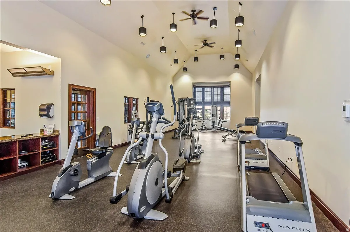 Fitness center featuring vaulted ceilings, recessed pendant lighting, rubberized flooring, and dark wood trim