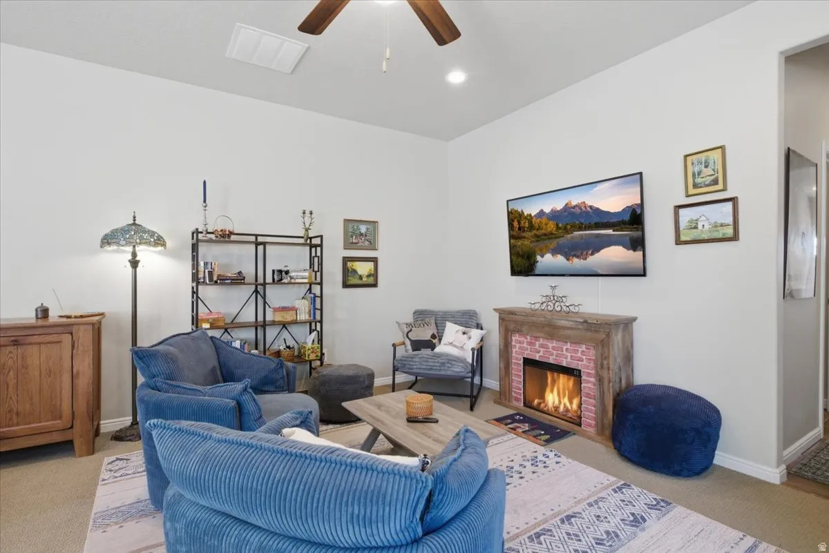 Living area featuring a ceiling fan, recessed lighting, wall-mounted television, and a fireplace with a brick-look surround