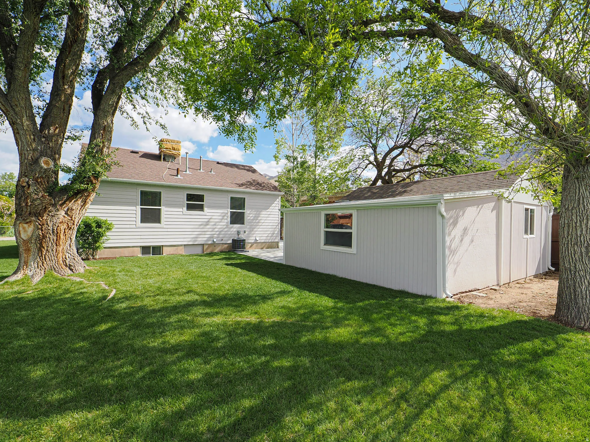 Expansive backyard featuring a green lawn, mature trees, and a detached outbuilding with multiple windows