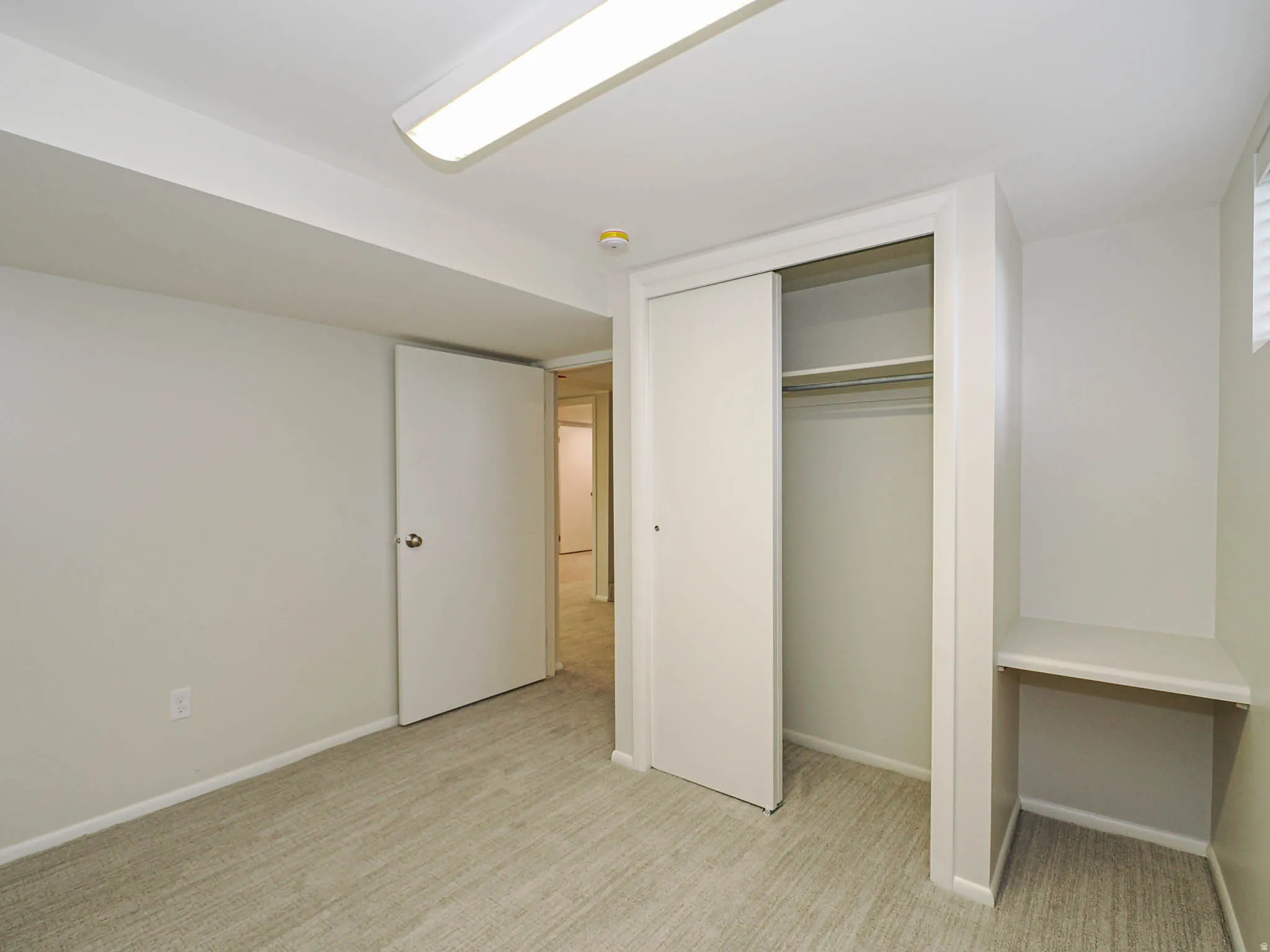 Carpeted room with a built-in closet featuring sliding doors, overhead LED lighting, and a built-in desk or shelving unit