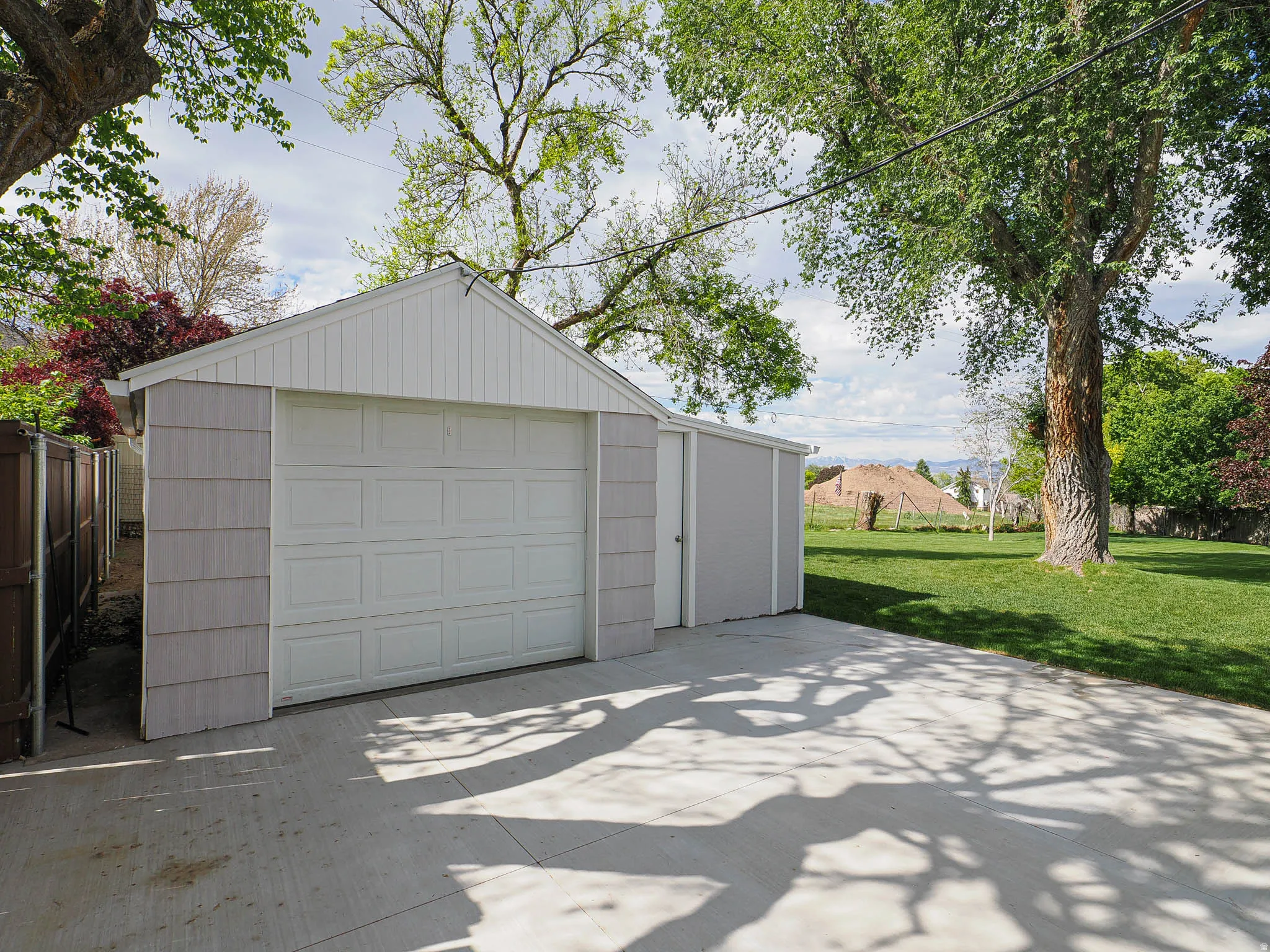 Detached garage with a paneled door, an adjacent storage shed, a concrete driveway, and an expansive lawn