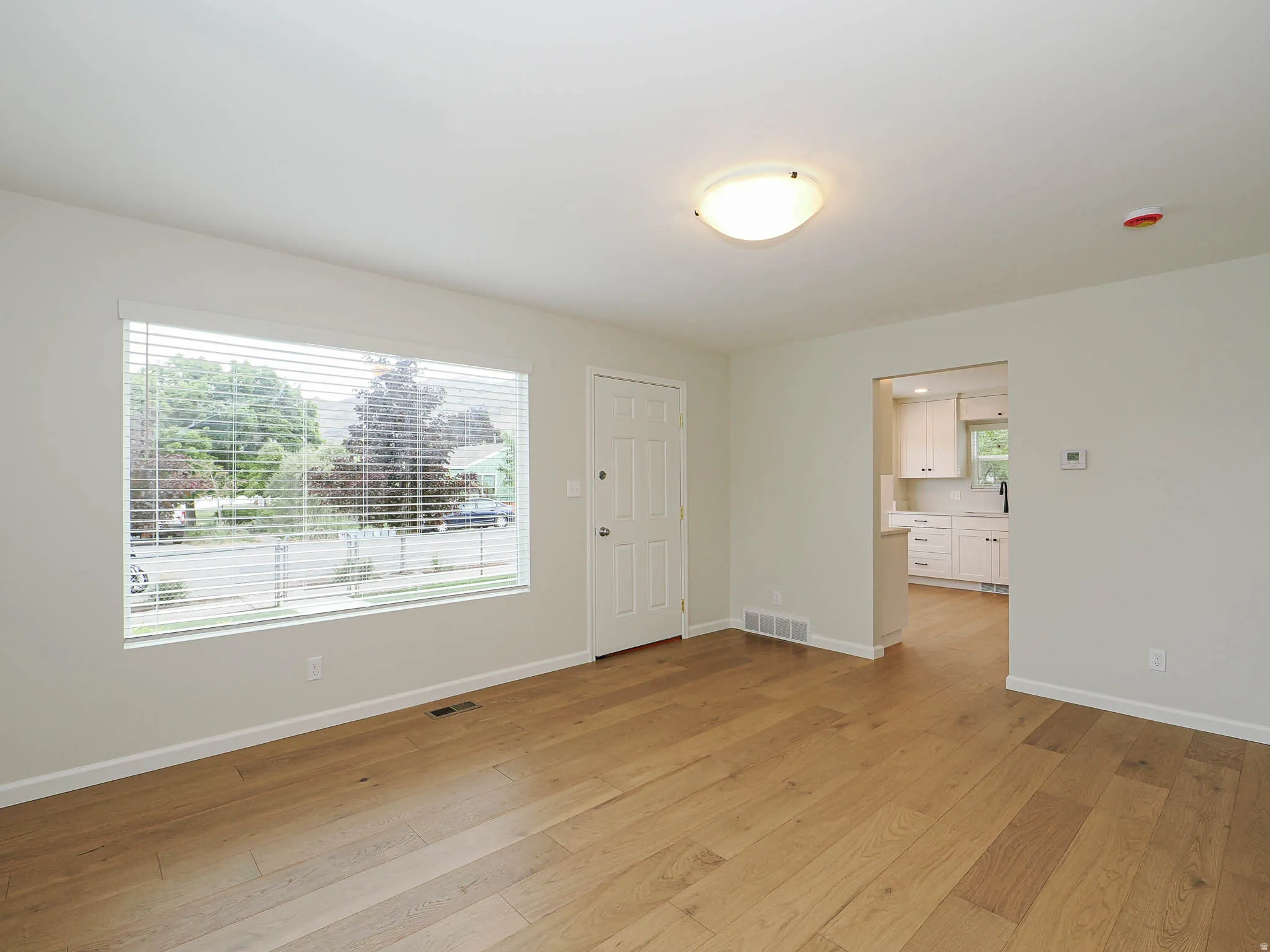 Spacious living area featuring wood-finish flooring, a large picture window with blinds, and recessed lighting