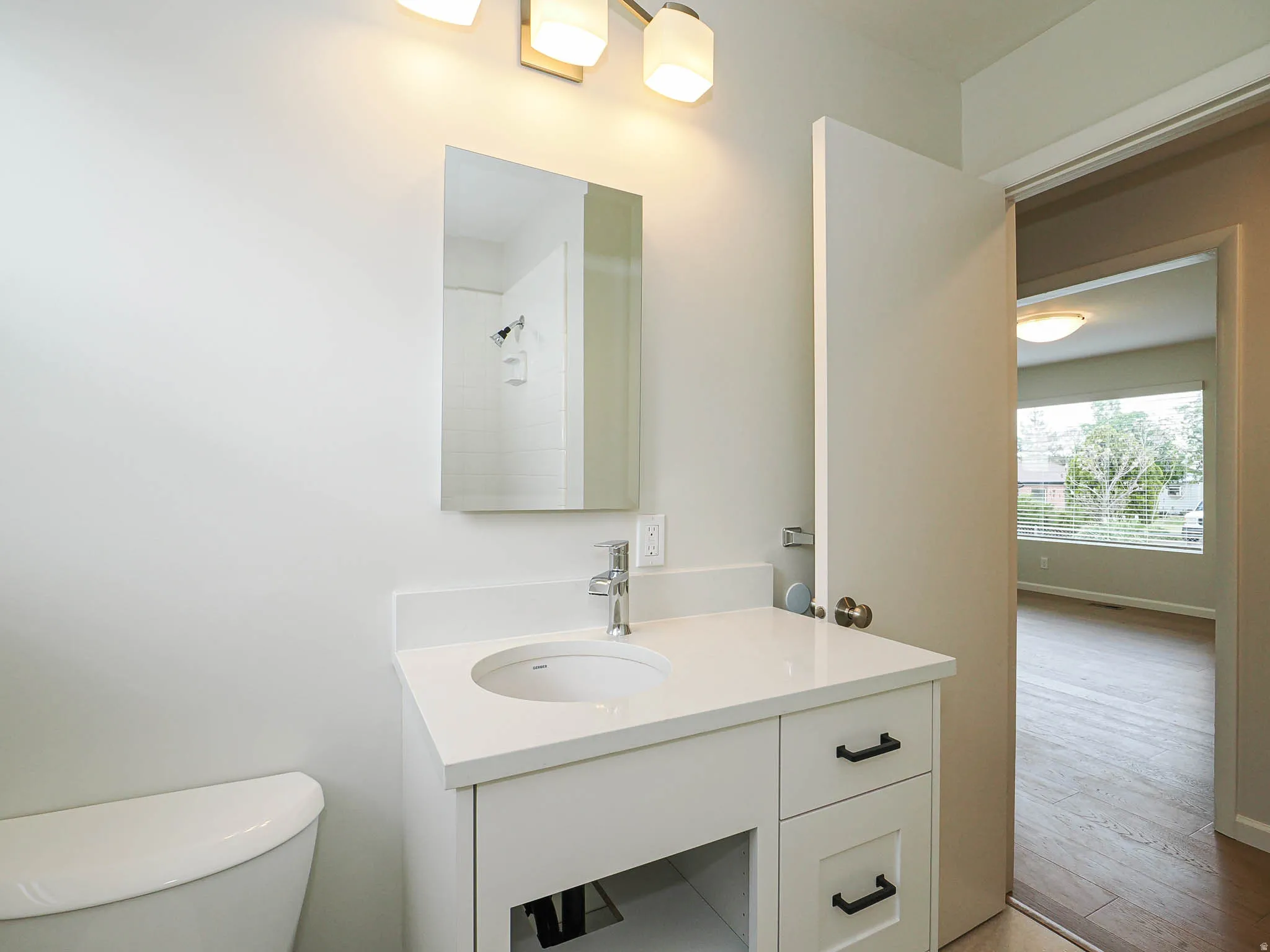 Bathroom featuring a white vanity with integrated sink, a sleek countertop, and a contemporary wall-mounted mirror
