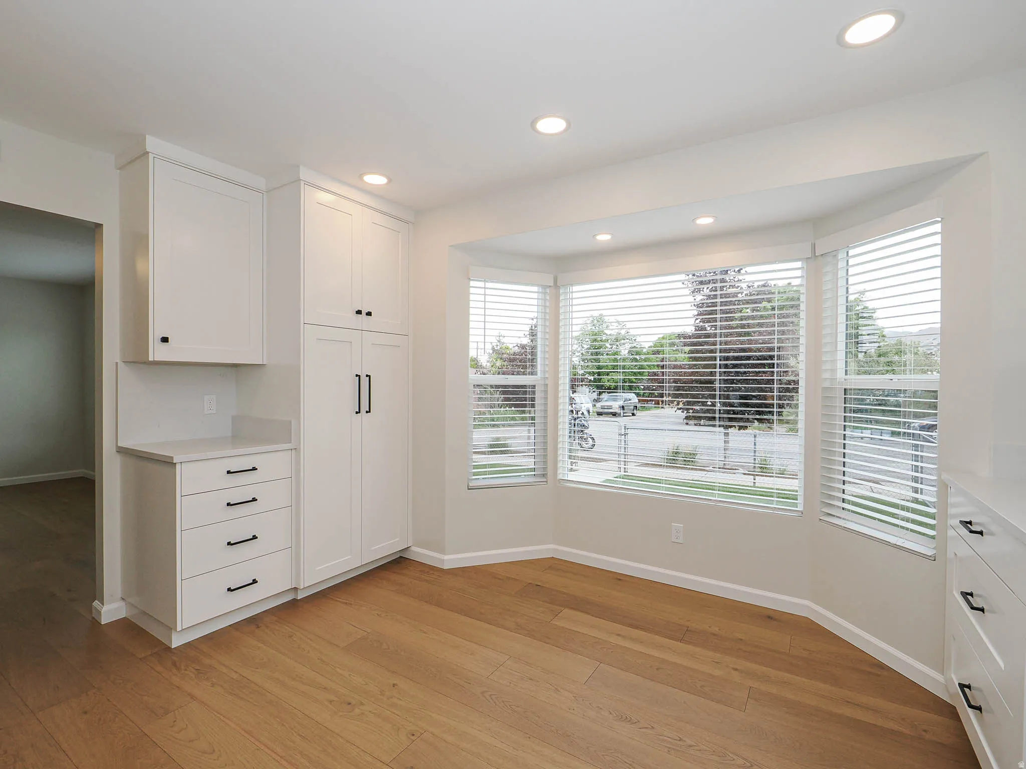 Bright room featuring a large bay window, recessed lighting, wood-finish flooring, white shaker cabinetry, and light-colored countertops