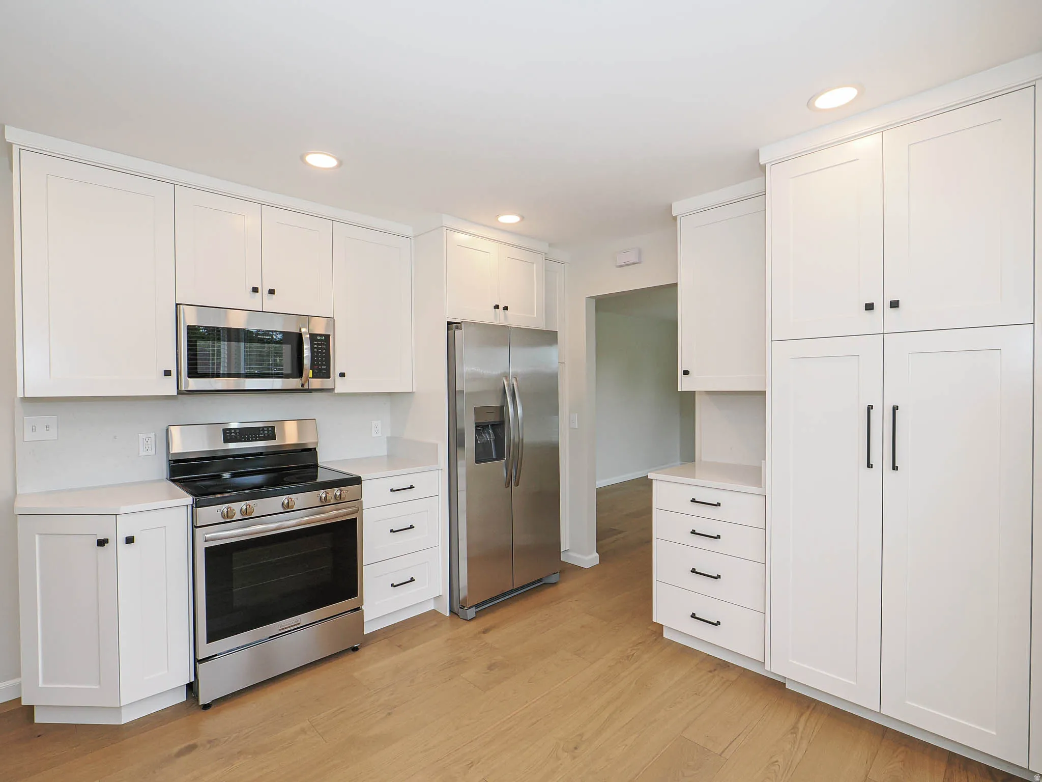 Kitchen featuring white shaker cabinetry, stainless steel appliances, light-toned countertops, and wood-finish flooring