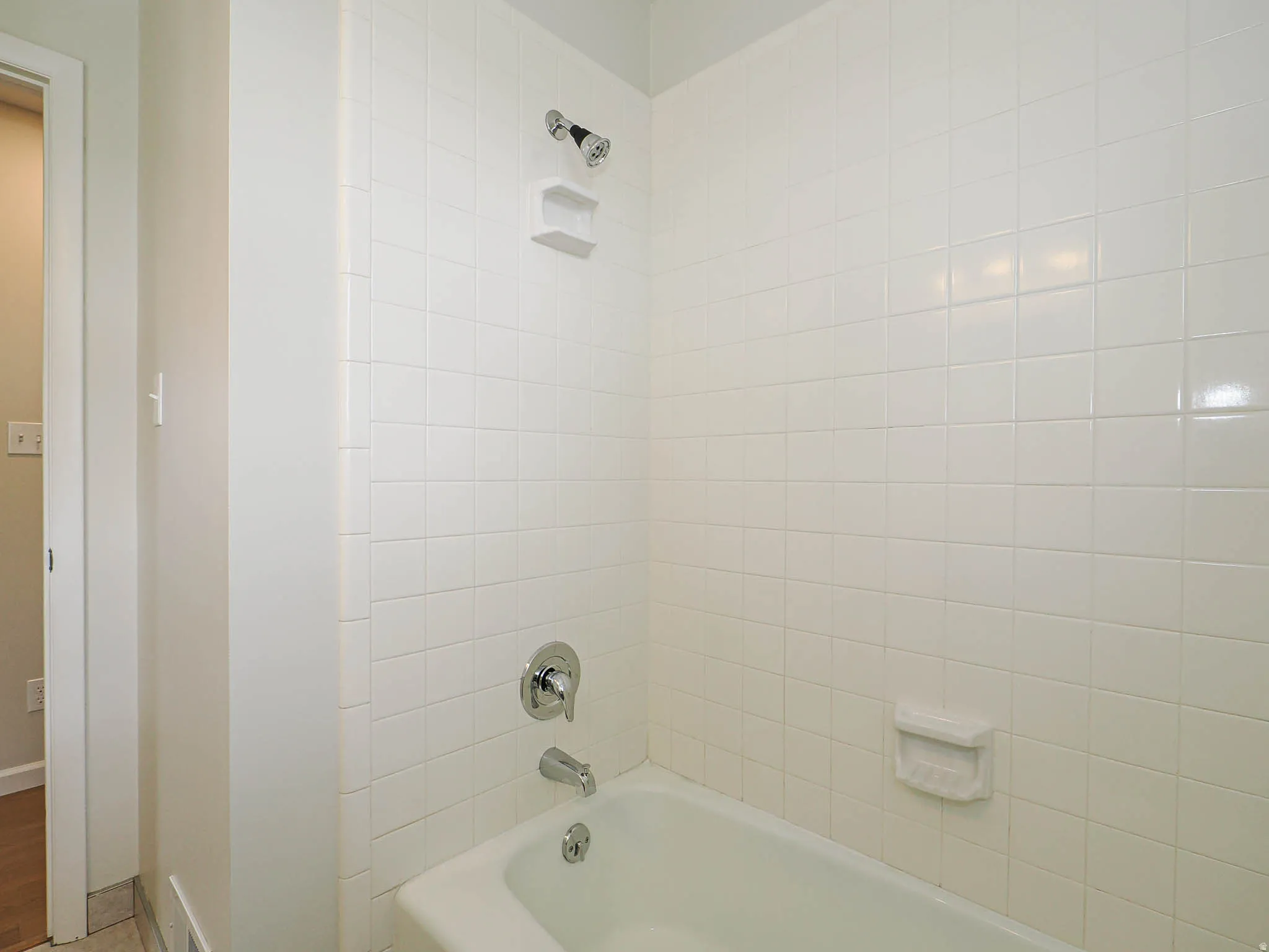 Bathtub with white tile surround, chrome showerhead, and chrome faucet