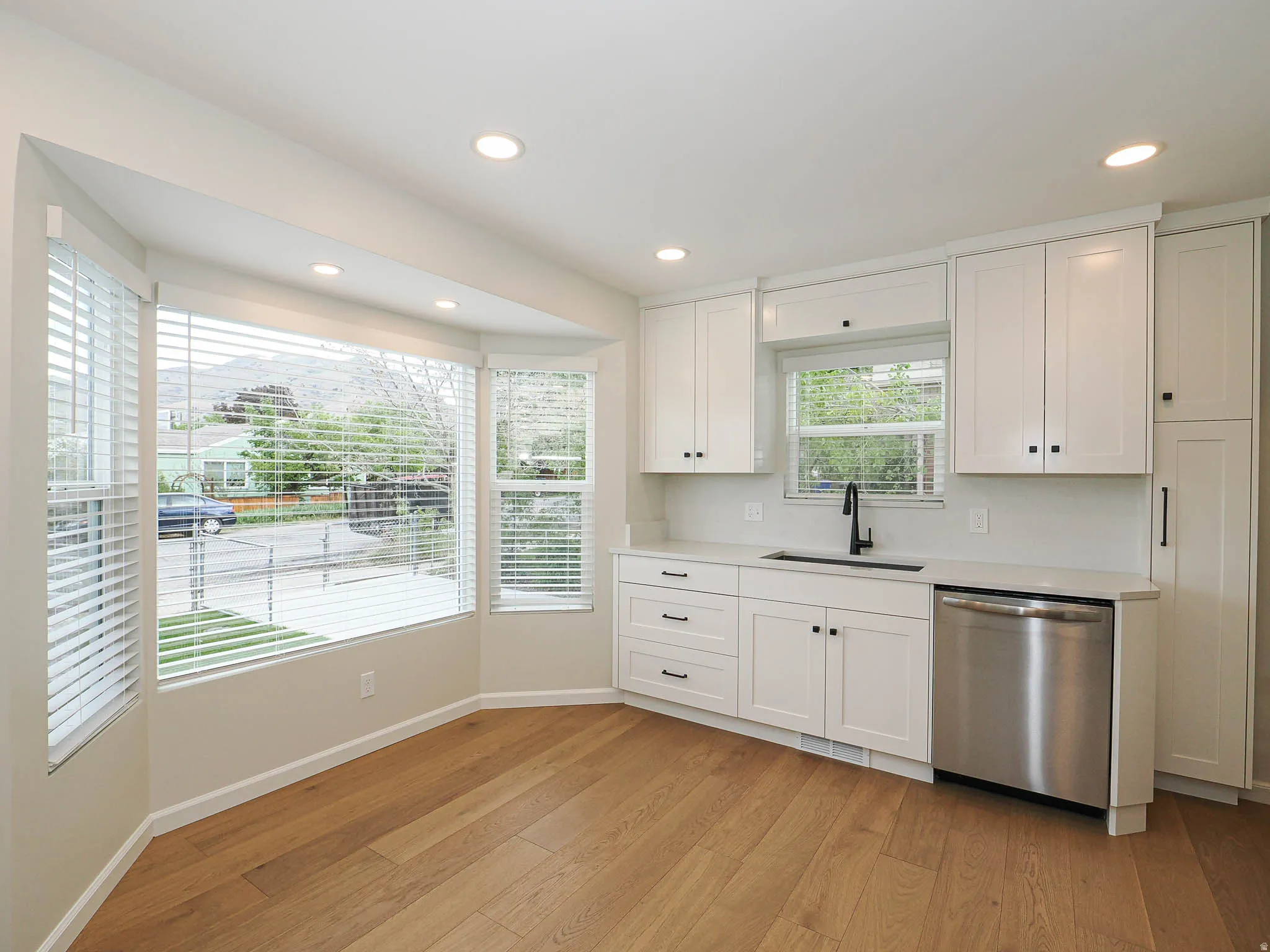 Kitchen featuring modern white cabinetry, light-toned wood-finish flooring, recessed lighting, and a bay window with blinds