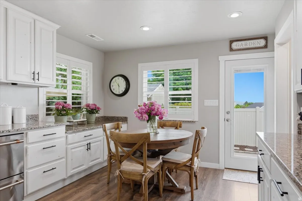 Kitchen dining area featuring white cabinetry, granite-style countertops, stainless steel appliances, wood-finish flooring, and a glass-paneled exterior door