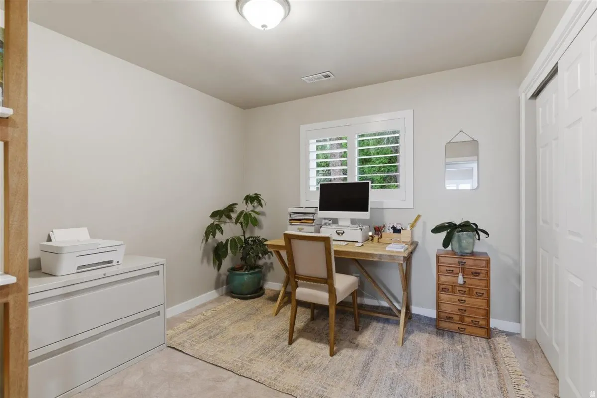 Bright interior room featuring a window with white plantation shutters, neutral wall paint, overhead flush-mount lighting, and light-toned carpet flooring