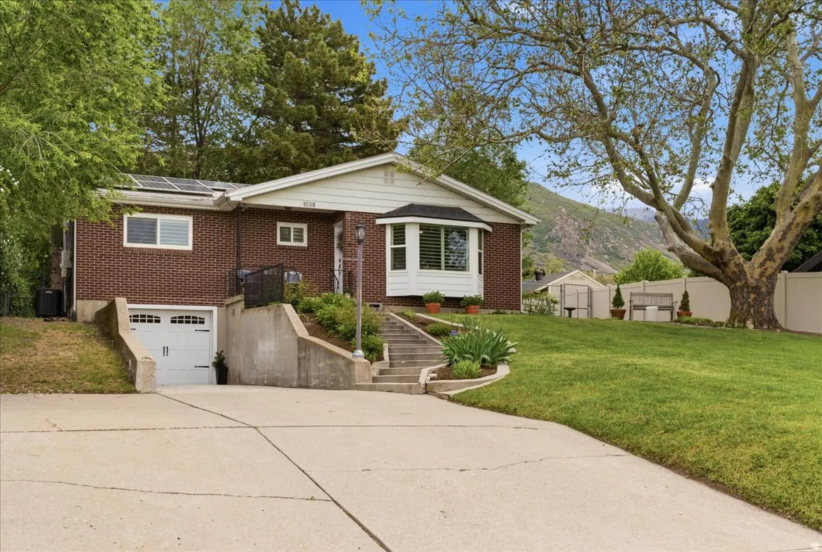 Traditional brick residence featuring a large front lawn, mature trees, a multi-pane bay window, solar panels, and a lower-level garage