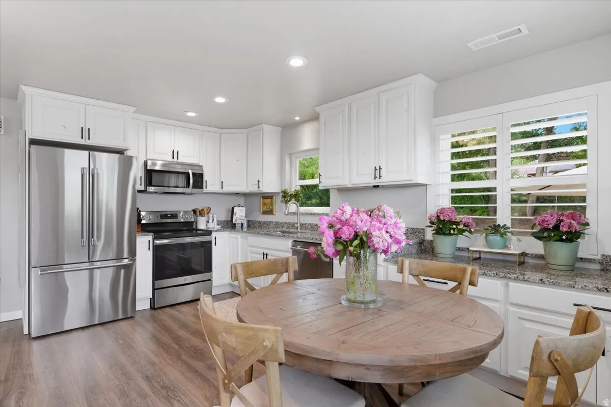 Kitchen featuring white cabinetry, stainless steel appliances, granite countertops, and wood-finish flooring