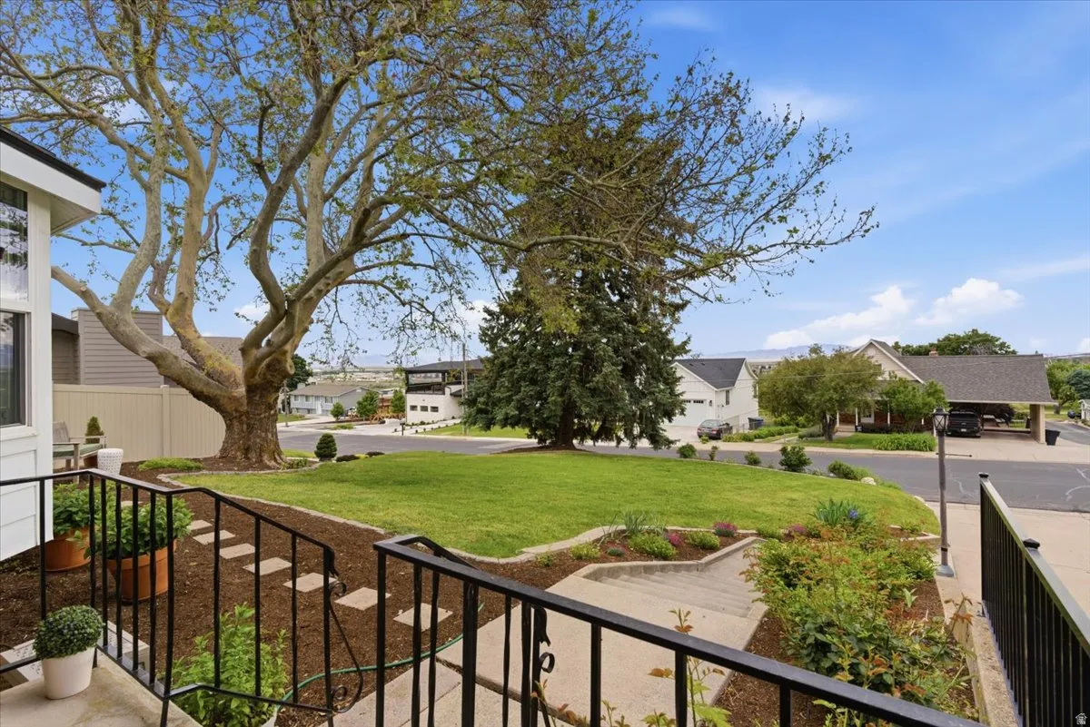 Front yard featuring a broad lawn, mature trees, and landscaping beds with ground cover