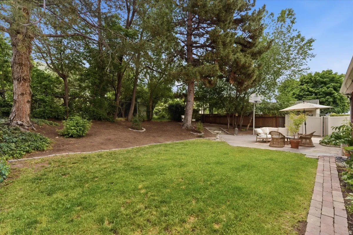 Expansive backyard featuring a lush lawn, mature trees, a paver patio, and a brick pathway