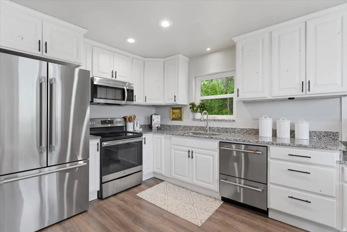 Kitchen featuring white cabinetry with dark hardware, granite countertops, stainless steel appliances, wood-finish flooring, and recessed lighting