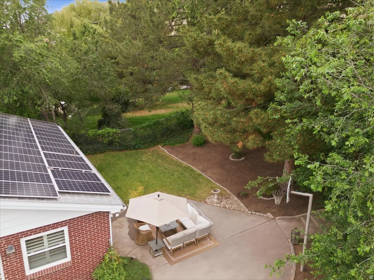 Brick exterior with solar panels, a paved patio, and a basketball hoop, surrounded by mature trees and a manicured lawn