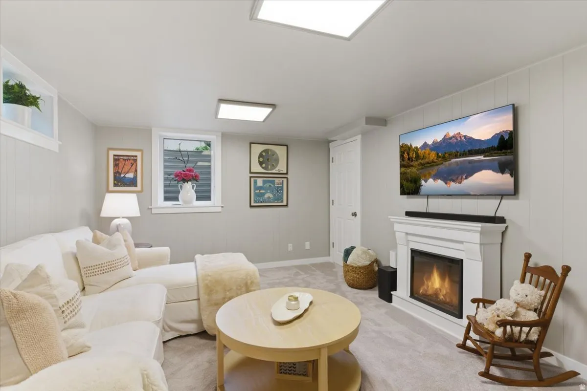 Carpeted living space featuring a fireplace with a white mantel, two rectangular ceiling-mounted light fixtures, and paneled wall finishes