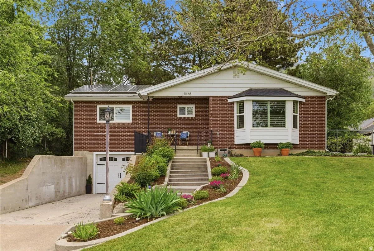 Brick exterior featuring a white bay window, solar panels, and a terraced front lawn with mature landscaping