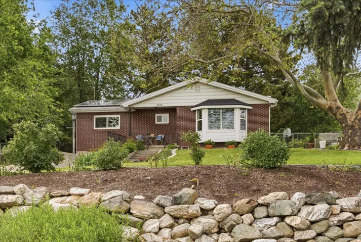 Brick exterior with a prominent bay window, a front porch with steps, solar panels, and a stone retaining wall