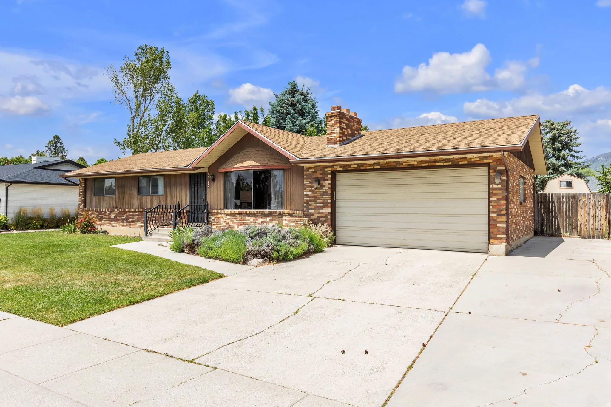 Ranch-style residence featuring a brick facade, wood siding, a front-facing garage, a concrete driveway, and established landscaping