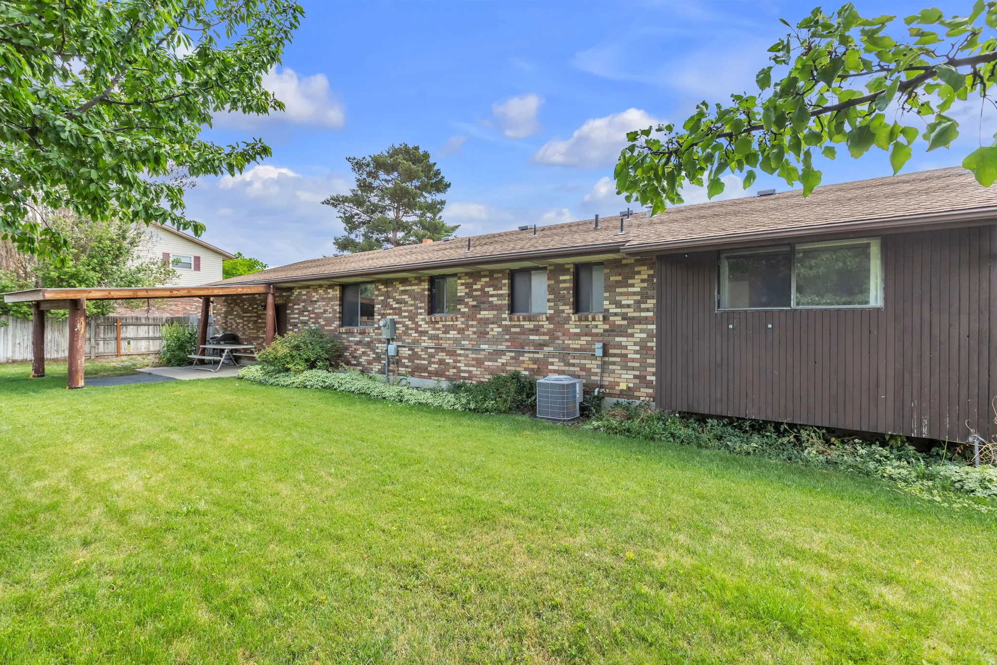 Expansive rear yard featuring a covered patio, brick exterior, natural wood pergola, mature trees, and a manicured lawn