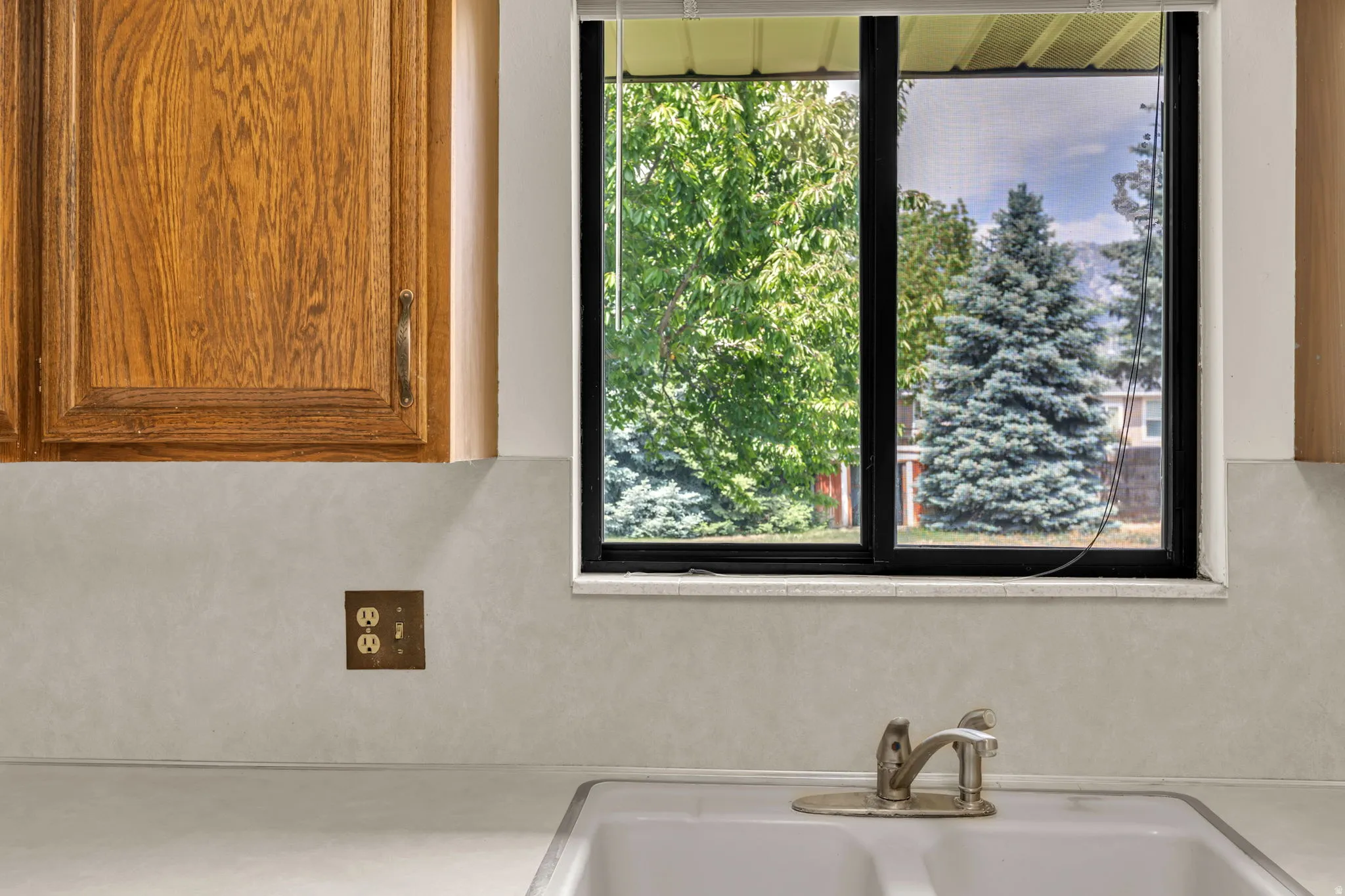 Kitchen sink with a dual basin, a single-handle faucet, and a large window overlooking mature trees