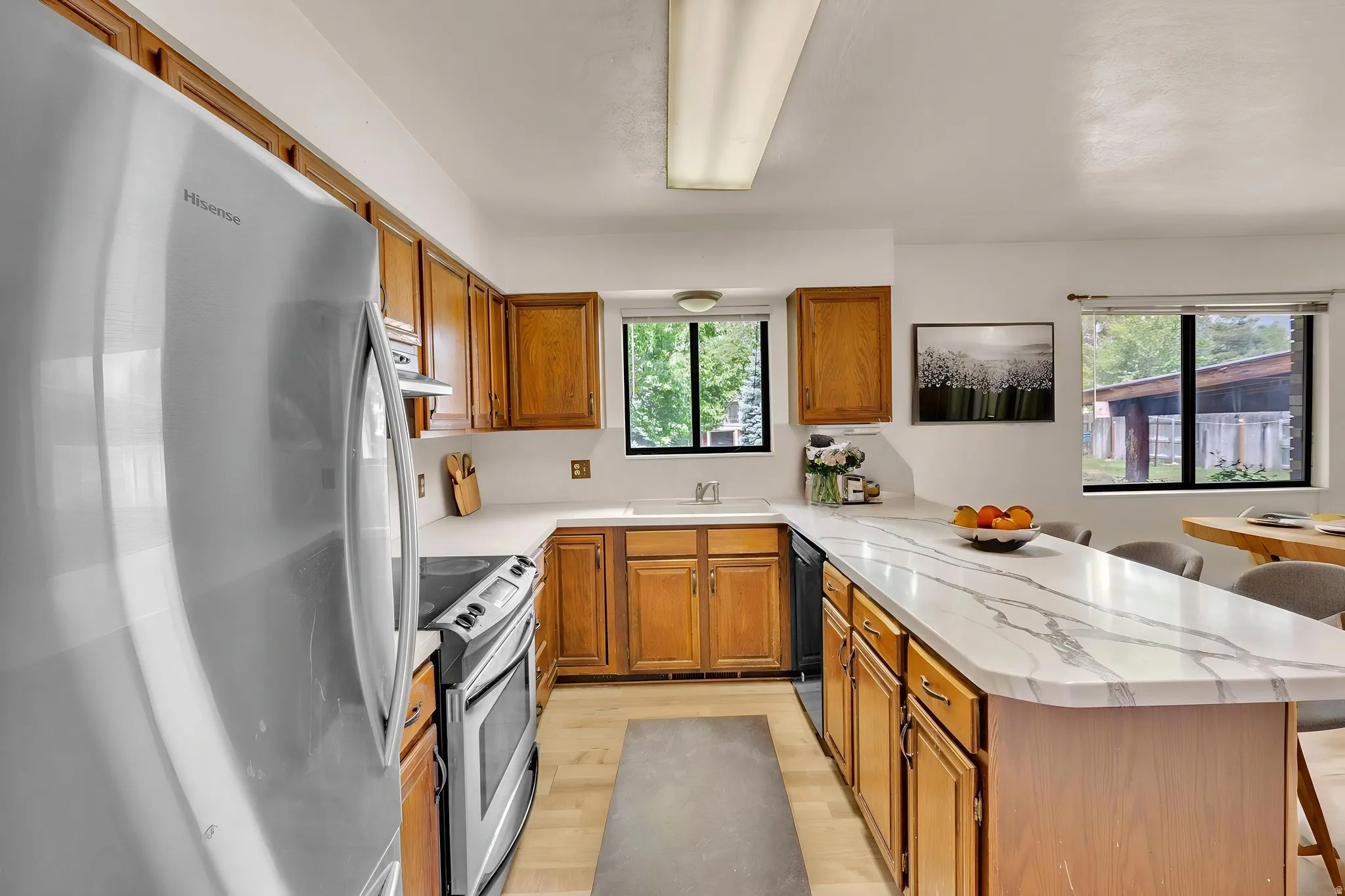 Virtually Staged -U-shaped kitchen featuring light wood cabinetry, white countertops with gray veining, light wood-finish flooring, and a stainless steel oven