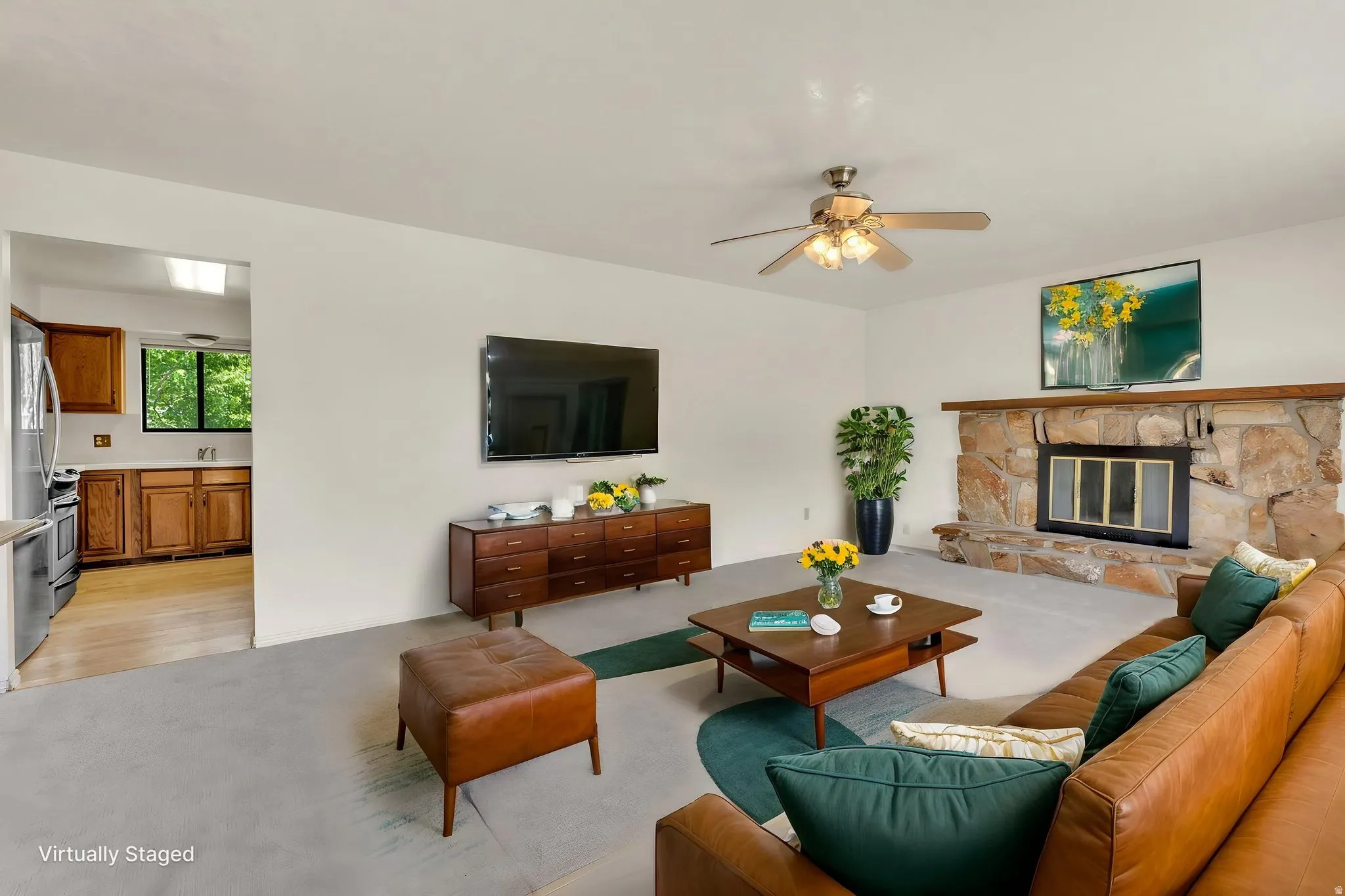 Virtually Staged -Living area featuring a stone-clad fireplace with a wood mantle, a ceiling fan, and carpet flooring